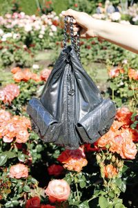 Black handbag held over blooming roses.