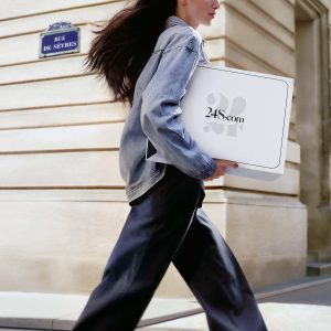 Person walking with 24S.com package on street.