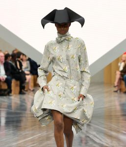 Model wearing gray floral outfit and unique black hat.