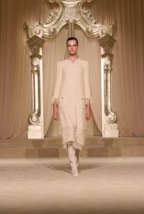 Model in white dress on ornate runway.